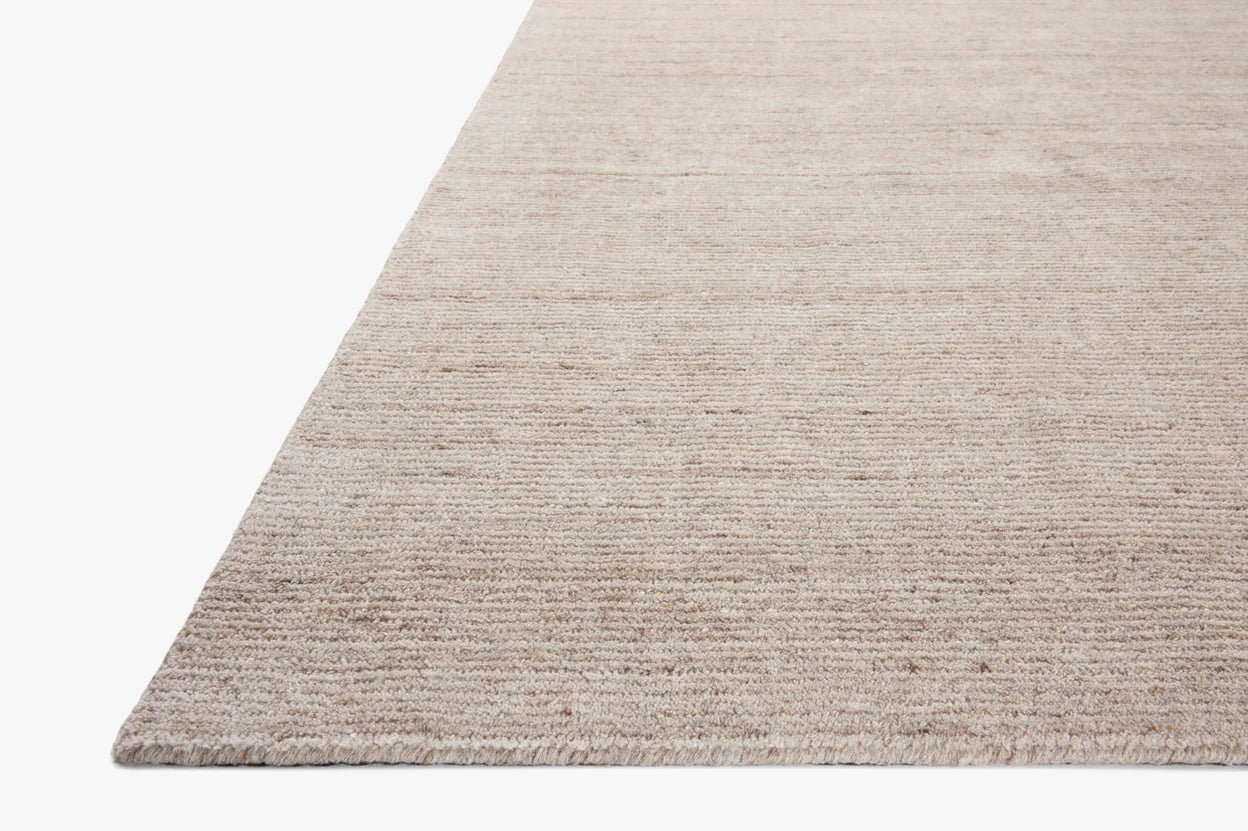 A close-up of the Color Block Rug - 8'-6" x 11'-6", featuring a beige, textured polyester pile with subtle horizontal lines. Shown on a white background with the edge in the lower left corner. Available in multiple sizes.