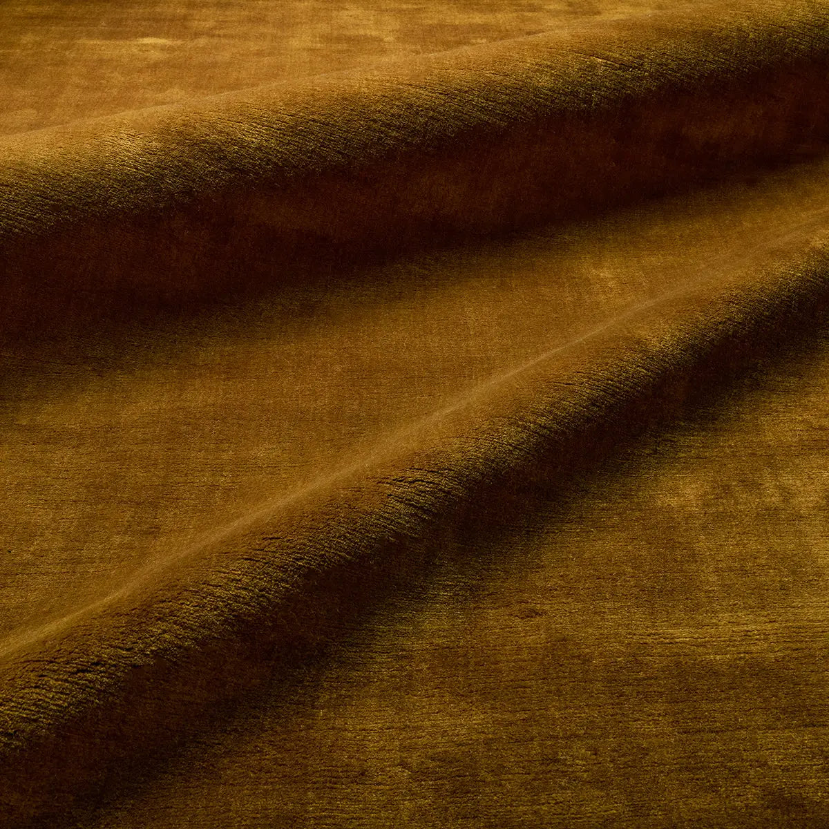 A close-up of soft, brown velvet fabric with gentle folds and shadows, highlighting its plush texture—evoking the luxurious feel of the Handwoven Golden Wool Rug, expertly crafted from premium New Zealand wool.