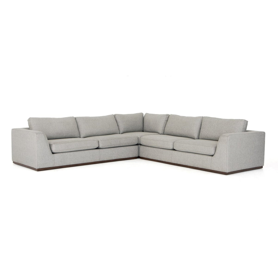 The Simple Modular Corner Sectional is a modern, light gray L-shaped sofa with clean lines, low backrests, plush cushioned seats in heirloom leather, and a dark wooden base, set against a plain white background.
