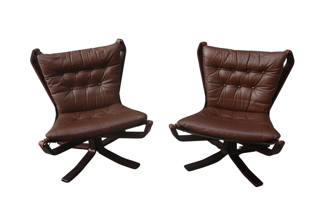 A pair of Vintage Falcon Chairs with dark brown tufted leather seats, curved wooden frames, and swivel bases are placed side by side against a white background—a classic Sigurd Ressell design.