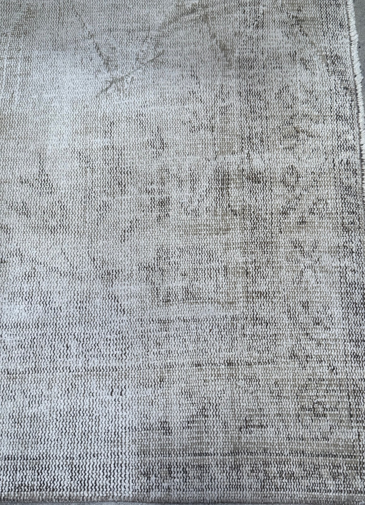 A close-up of the Vintage Cream/Grey Turkish Rug, featuring a light gray and beige woven design with a subtle, faded pattern and slightly frayed edges. This piece measures 8'8" x 5'3".