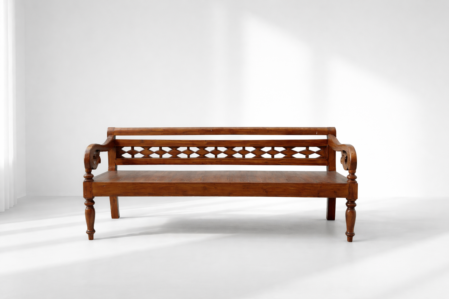 The Vintage Wood Carved Bench (78Wx23Hx25.5D), featuring carved armrests and a decorative backrest, sits in a bright minimalist room with white walls and sunlight streaming through the window.