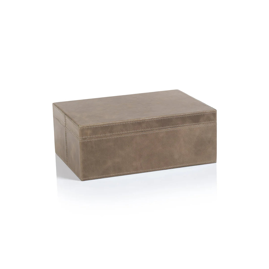 The Mink Leather Box is a small, rectangular brown leather box with visible stitching, closed and placed on a white surface that shows its faint reflection.