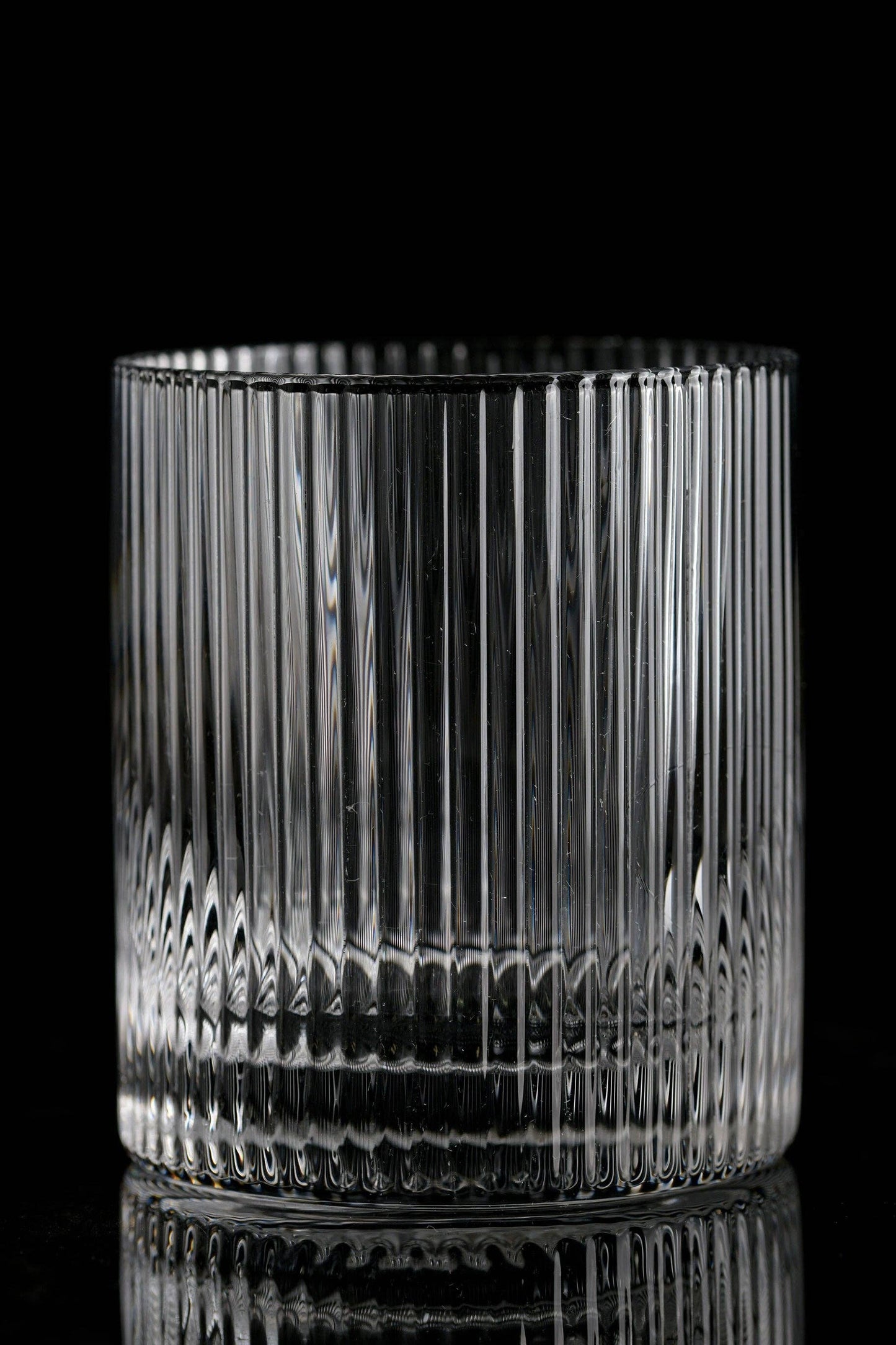 The Vintage Straight Line Tumbler - 10 oz (1pc) features clear glass with vertical grooves, displayed on a reflective black surface against a black background to highlight its classic, timeless elegance.