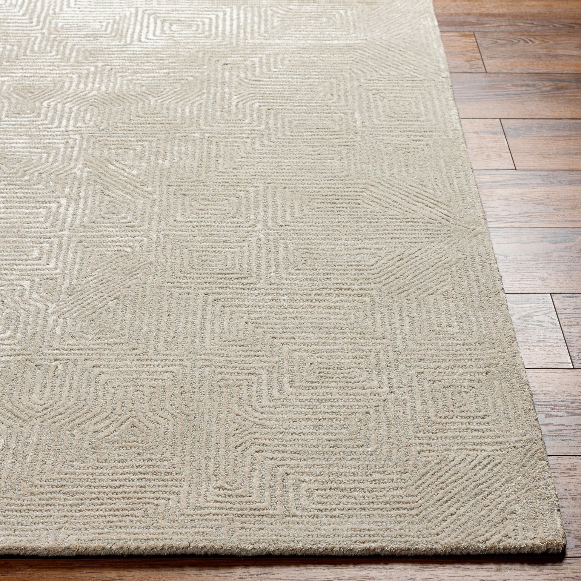 The Monochrome Maze Rug - 8 x 10 features a beige color with a subtle geometric maze pattern, offering a soft texture and modern design on a wooden floor.