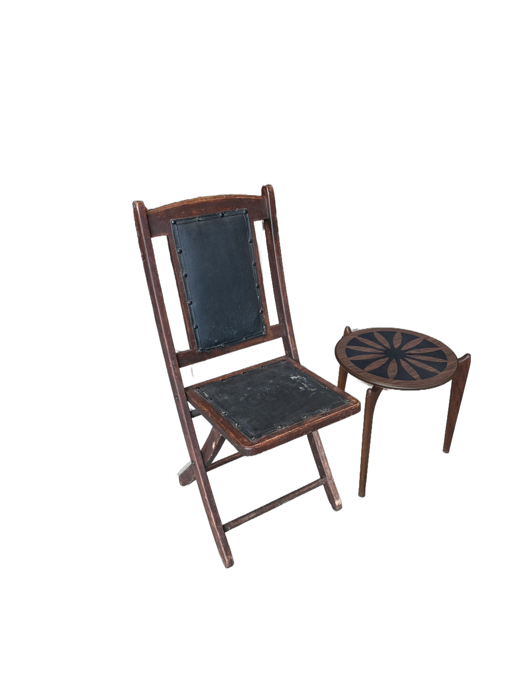 A Vintage Leather Folding Chair sits beside a small round wooden side table with a decorative sunburst pattern on the top.