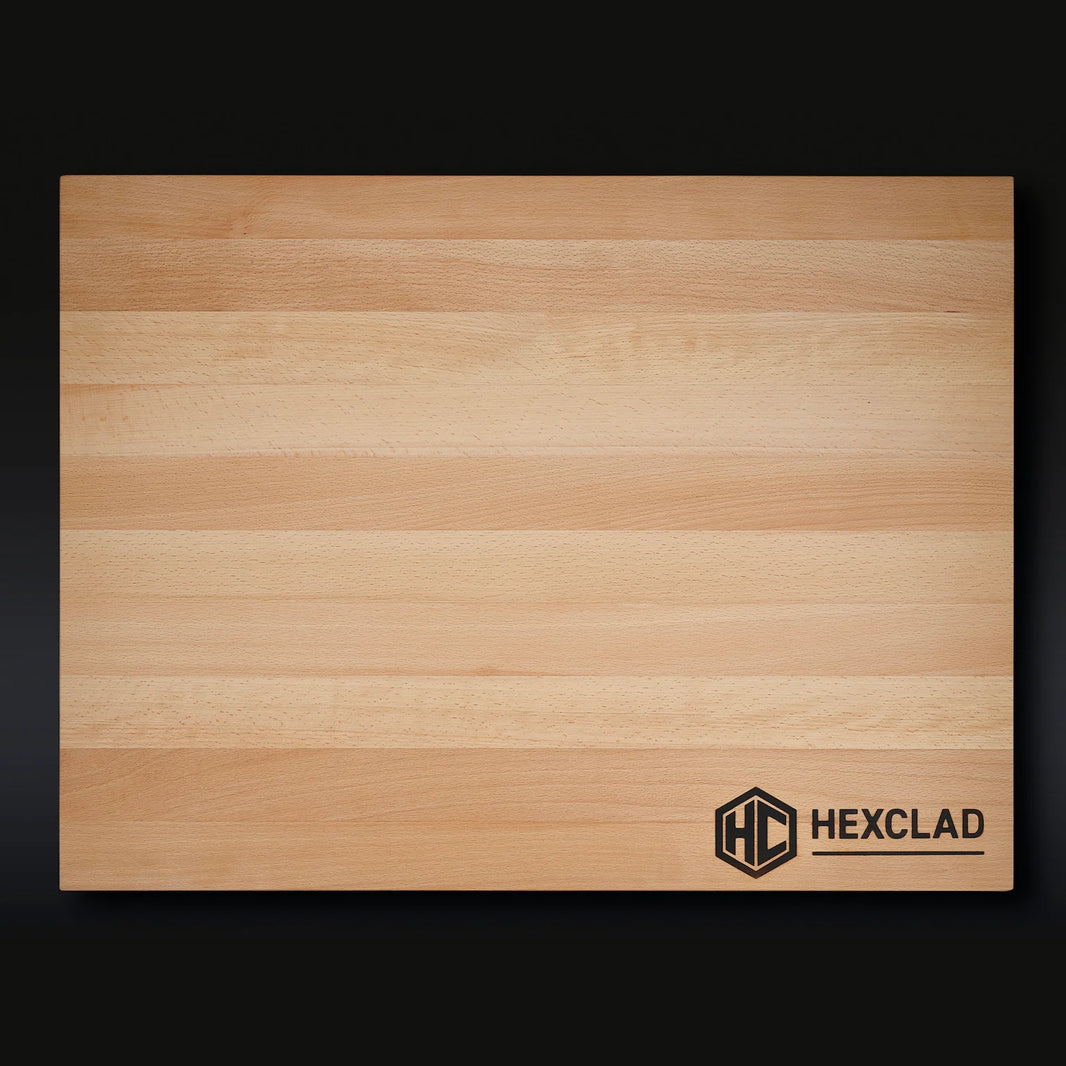 The HexClad XL Cutting Board is a rectangular beechwood board with light and medium stripes and a black HexClad logo on the bottom right, shown against a dark background.