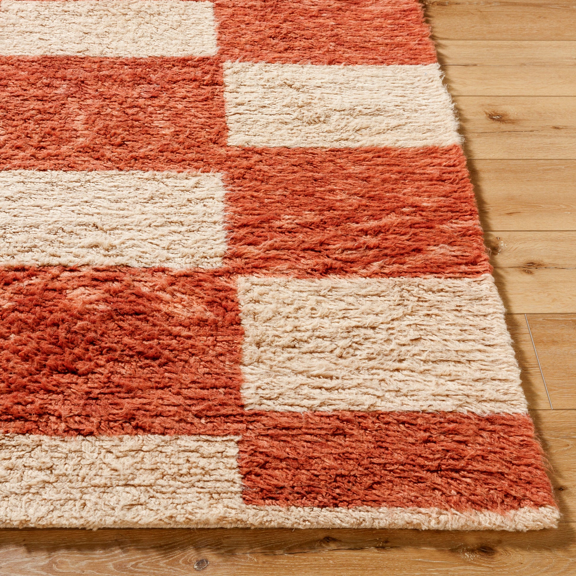 A close-up of the Camel Checkered Shag Rug (8 x 10), featuring a red and white checkerboard pattern, displayed on a light wooden floor.