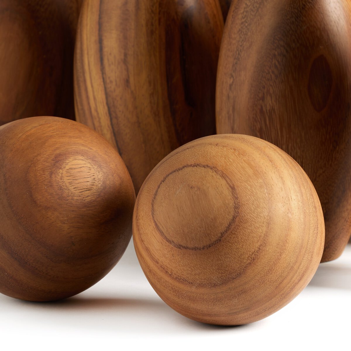 Three smooth wooden ovals with natural grain patterns are showcased in front of several Outdoor Bowling Set pins, all displayed on a white surface—ideal for an elegant solid wood bowling experience.