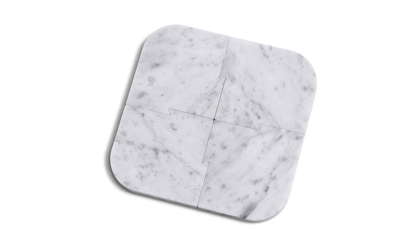 The Marble Coasters + Trivet set includes four interlocking, rounded-corner marble trivets in light gray with dark veining—perfect to pair with matching coasters and a chic walnut stand for a stylish tabletop.
