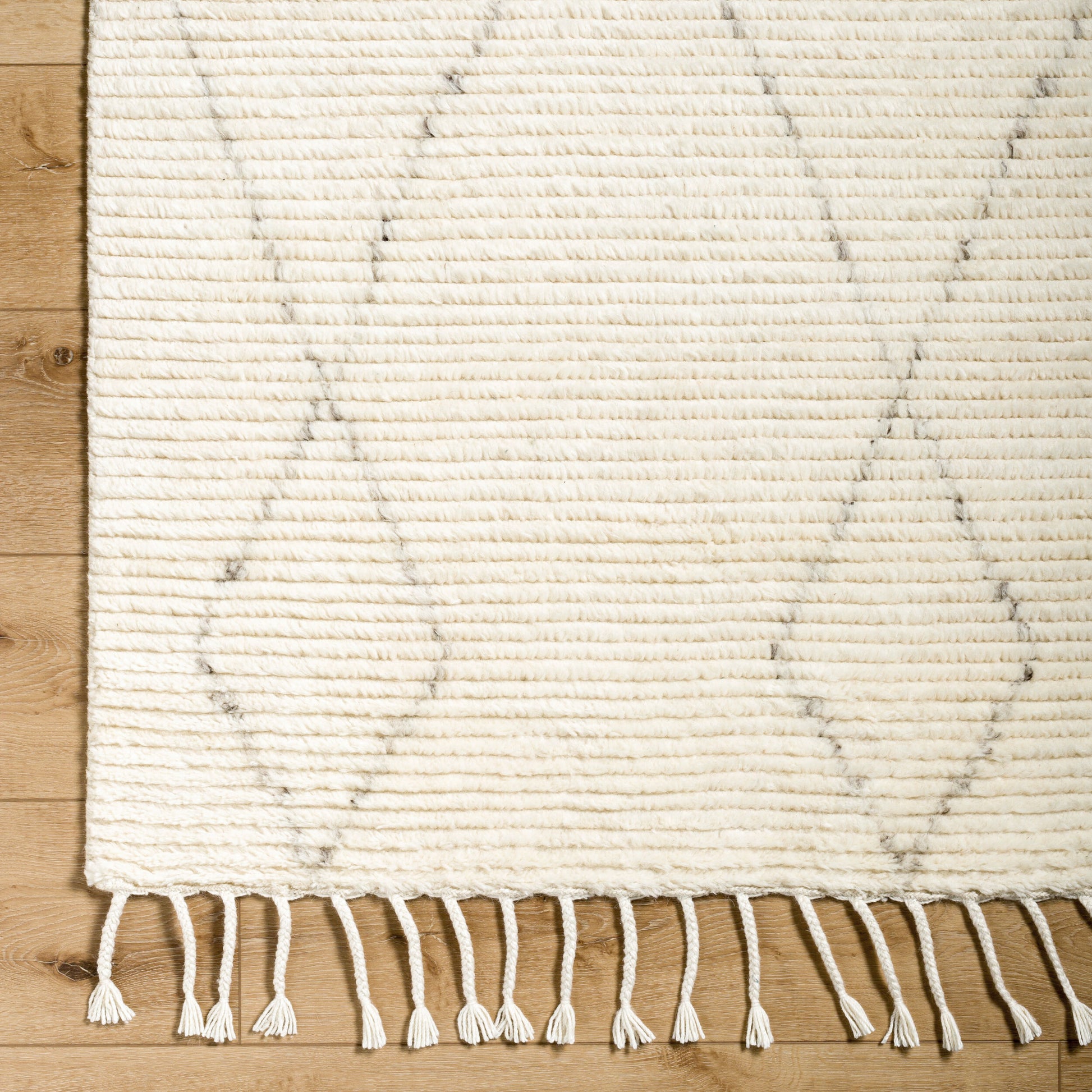 The Mid Century Mid Pile Rug - 8'x10' features a cream color with subtle gray diamond patterns, horizontal textured lines, and twisted fringe tassels along the edges, available in various sizes for placement on wooden floors.