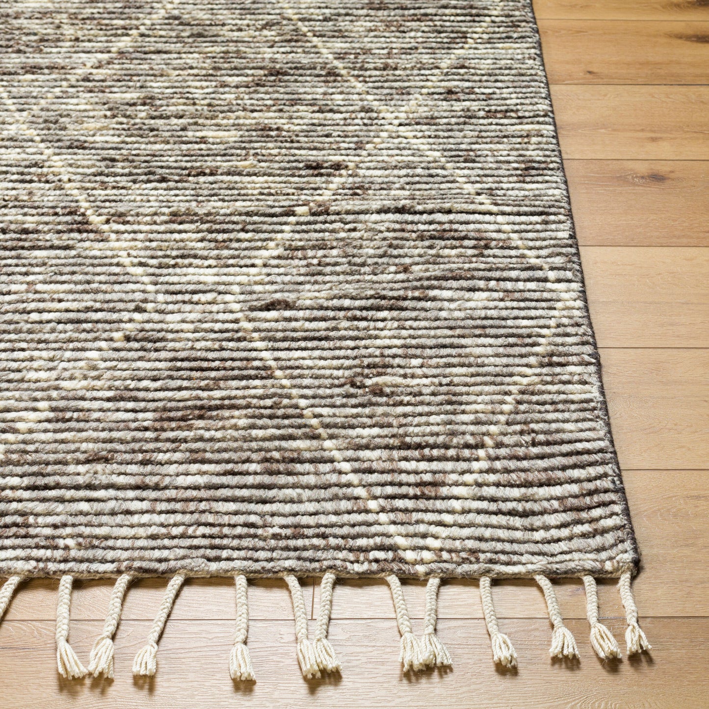 A close-up of the Mid Century Mid Pile Rug (8'x10') in cream and brown with a diamond pattern and cream fringes, shown on a light wooden floor; available in multiple sizes.