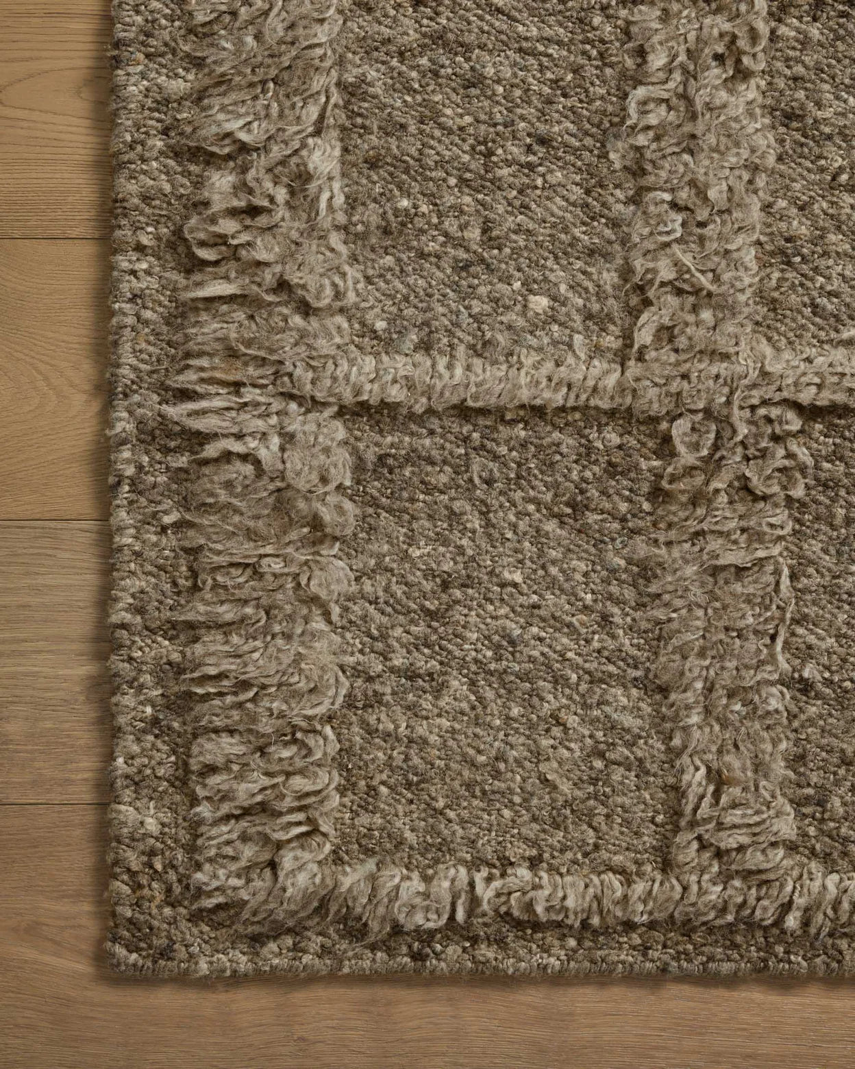 A close-up of the Wool Shag Squares Rug 8'6x11'6 in Sage, featuring a textured rectangular design with a grid pattern and fringed lines, placed on a light wood floor.