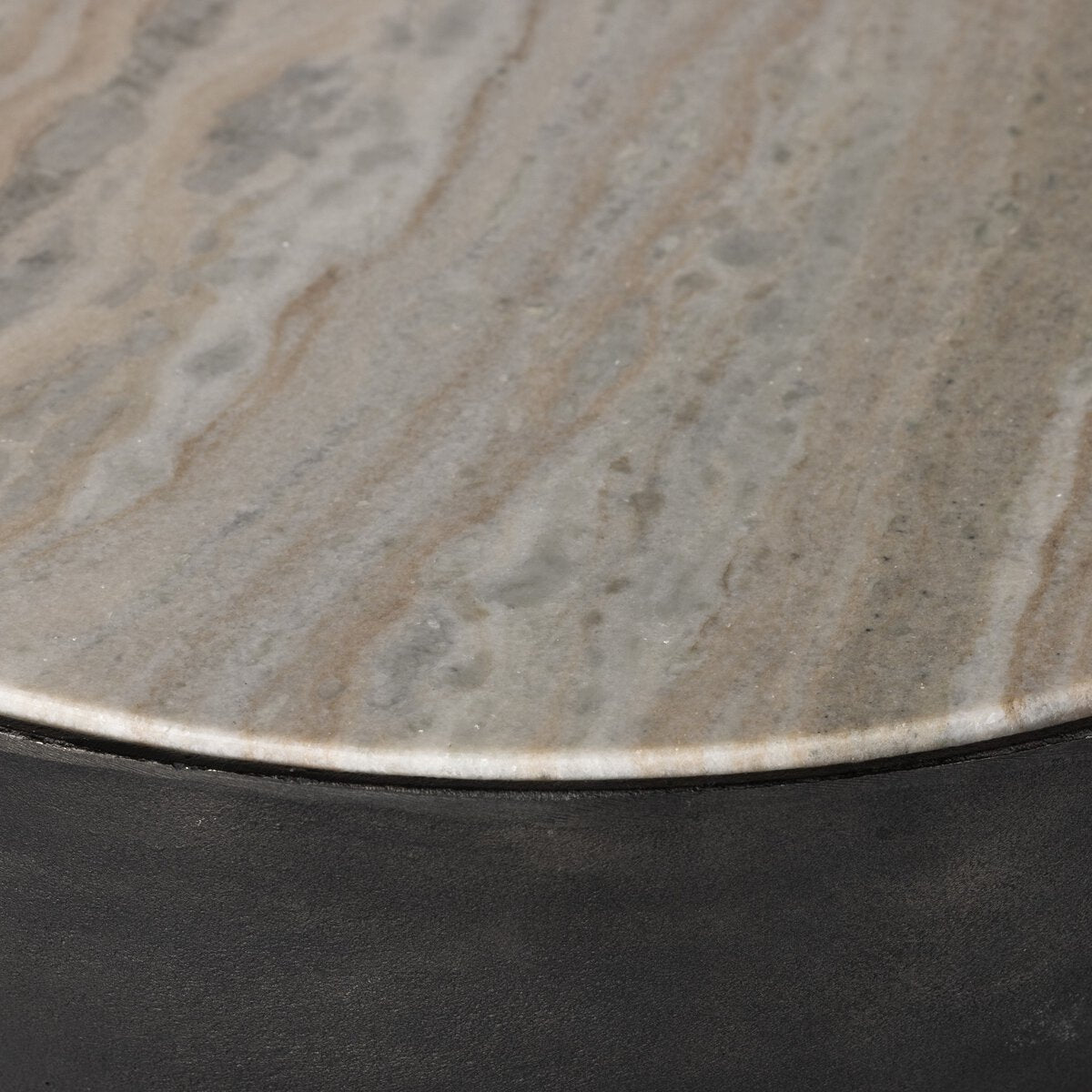 The Aluminum And Marble End Table features a polished marble tabletop with natural beige and gray veining, set on a dark, matte hammered aluminum base.