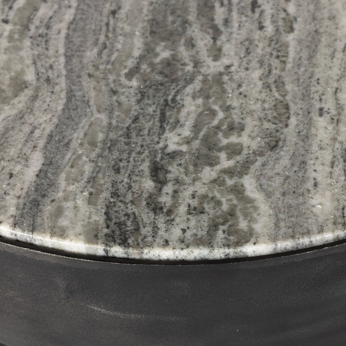 Close-up of the Aluminum And Marble End Table, featuring a polished gray and white marble top with natural veining and wavy patterns. The rounded edge highlights the dark hammered aluminum base beneath.
