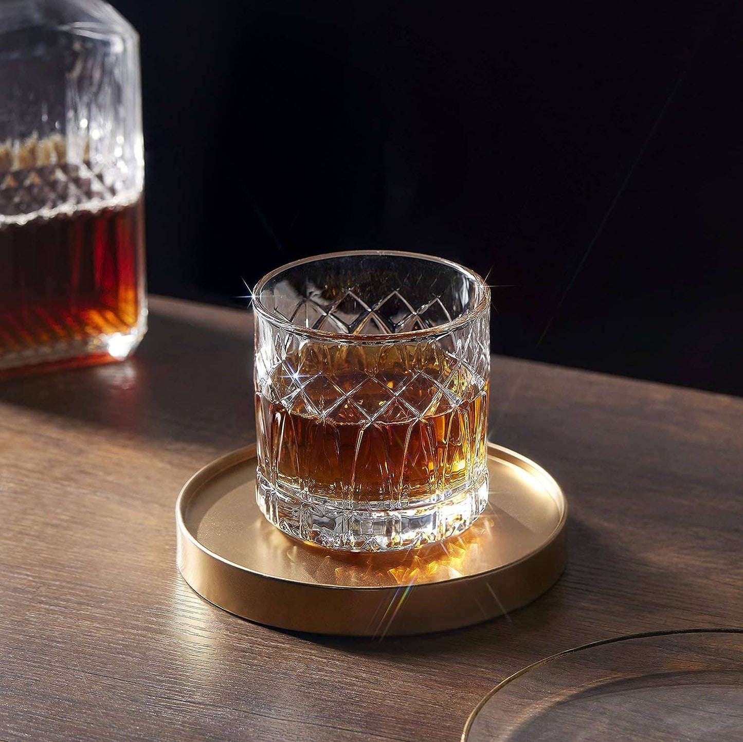 A LEMONSODA Premium Double Rocks Whiskey Glass (12oz) sits on a round gold tray atop a wooden surface, adding elegance to any home bar. A matching crystal decanter in the background enhances the allure of fine glassware.