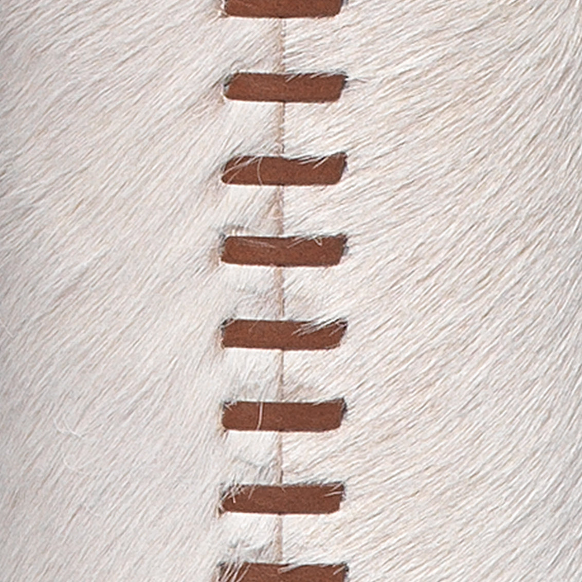 Close-up of white cowhide featuring brown leather strips woven in a zigzag pattern down the center—an artisanal stitched seam detail characteristic of the Stitched Cowhide Floor Lamp.