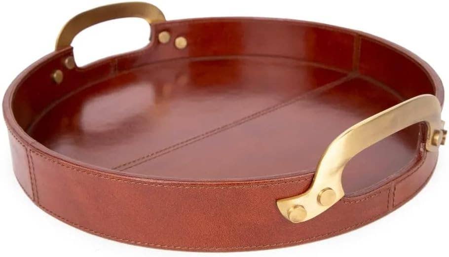 The Vintage Genuine Leather Tray is a round, brown leather tray with brass handles on opposite sides and a stitched seam detail across the base.