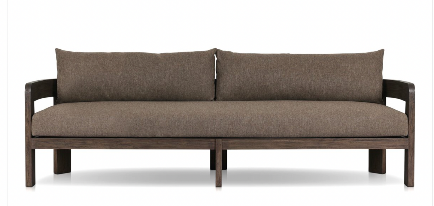 The Jackson Outdoor Sofa is a modern piece with brown upholstery and teak frame, featuring two back cushions, a wide seat, minimalist straight lines, and open armrests.