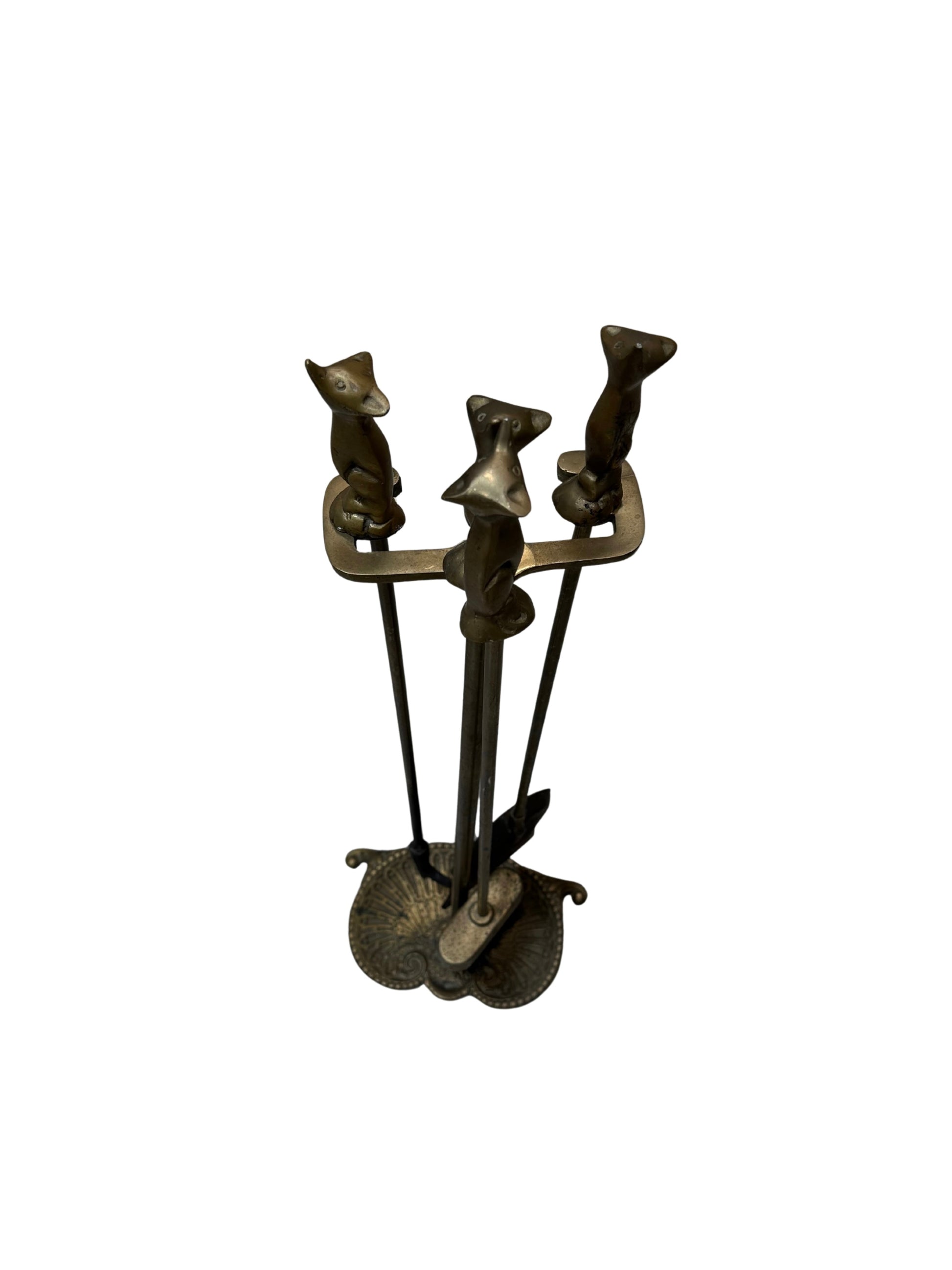 The Brass Chimney Set features brass fireplace tools with handles shaped like animal heads, possibly foxes, arranged upright on a decorative base against a white background.
