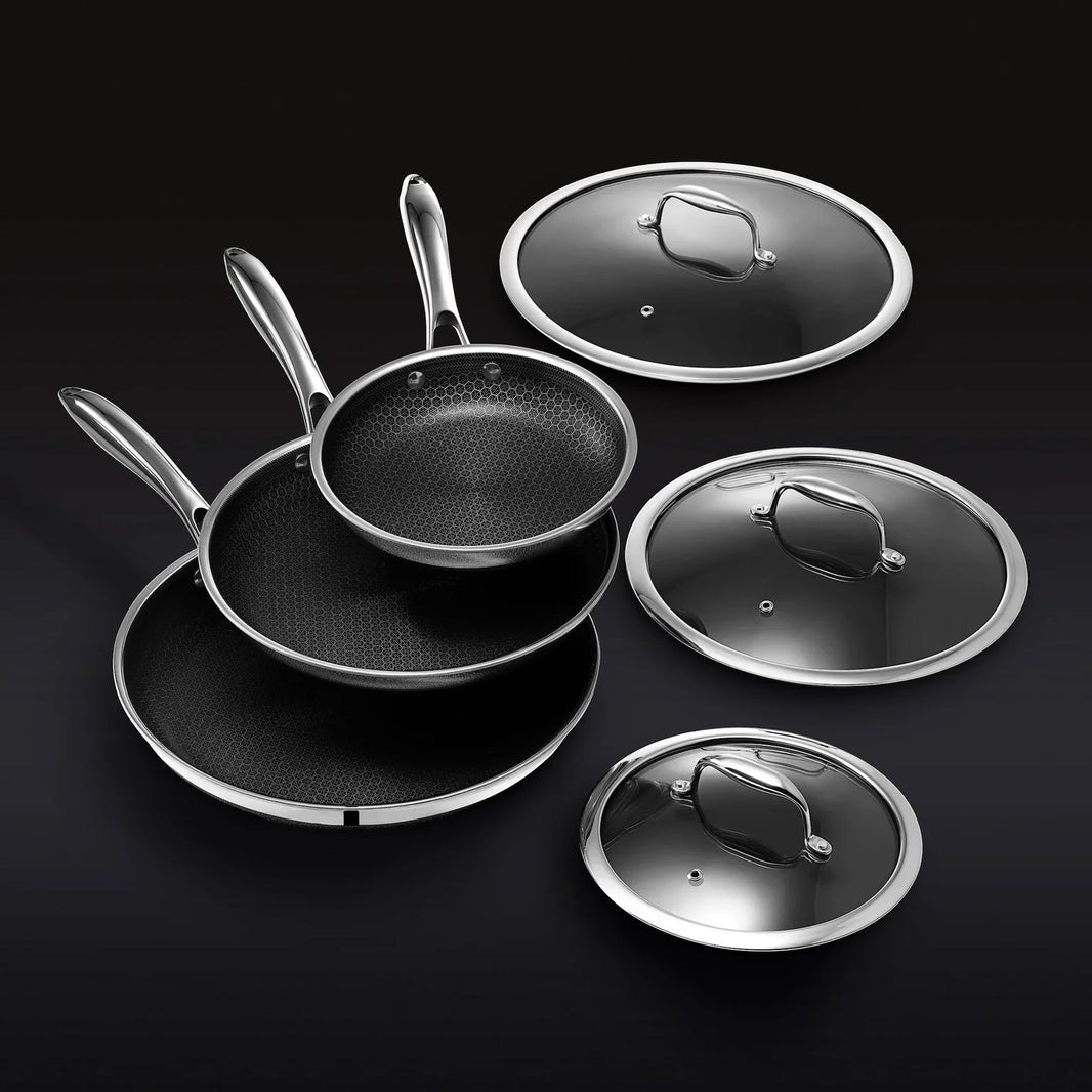 The Hexclad Fry Pan Set with Lids features three nonstick pans with metal handles, stacked together beside matching glass lids, all elegantly arranged against a black background.