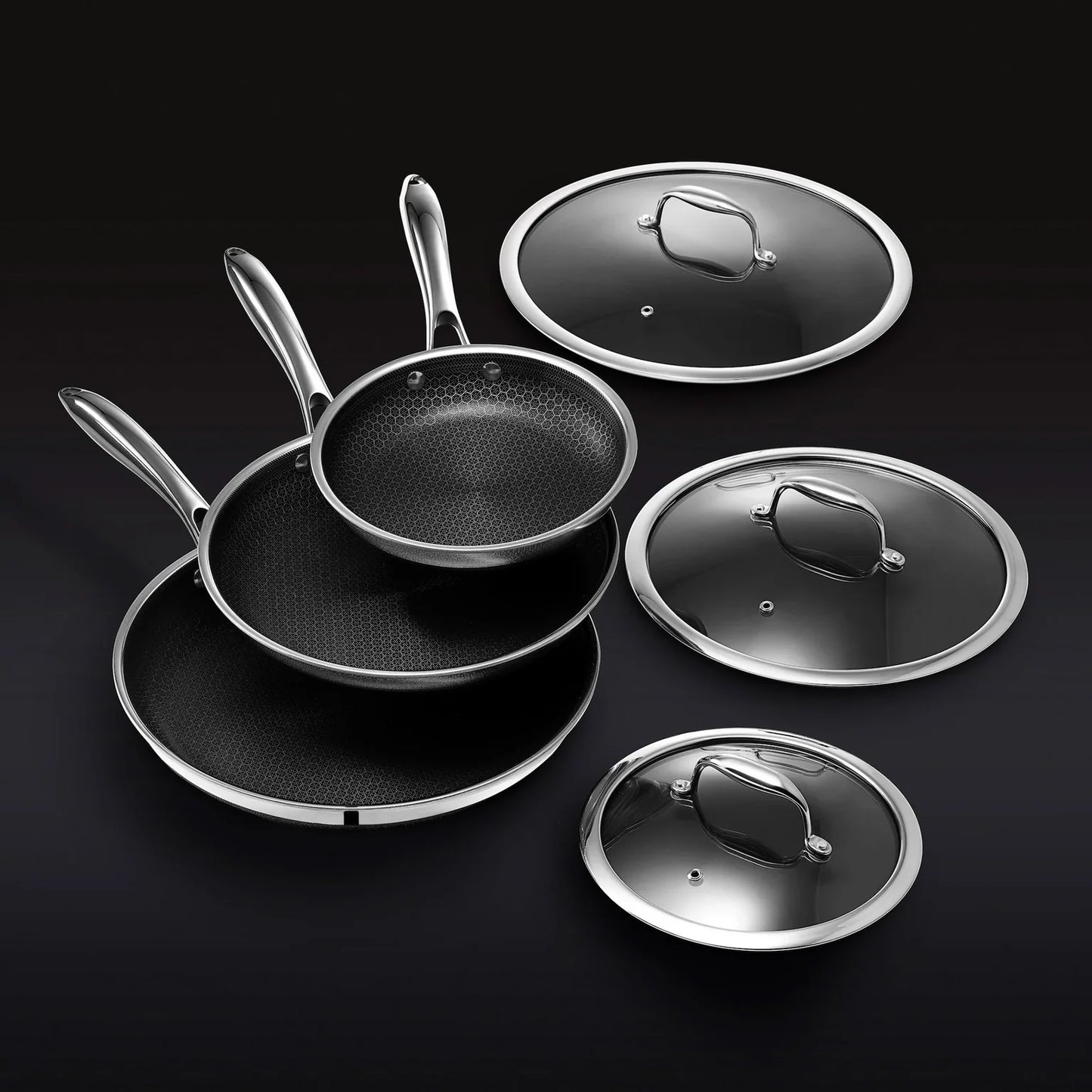 The Hexclad Fry Pan Set with Lids features three nonstick pans with metal handles, stacked together beside matching glass lids, all elegantly arranged against a black background.