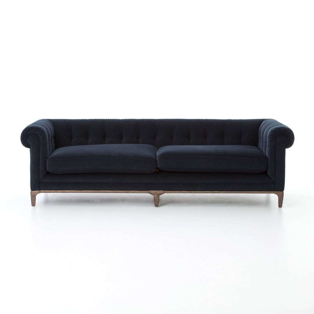 The Chesterfield Navy Sofa features dark navy blue upholstery, tufted detailing, rolled arms, and wooden legs. Set against a white background, its classic design and elegant dimensions are accentuated.