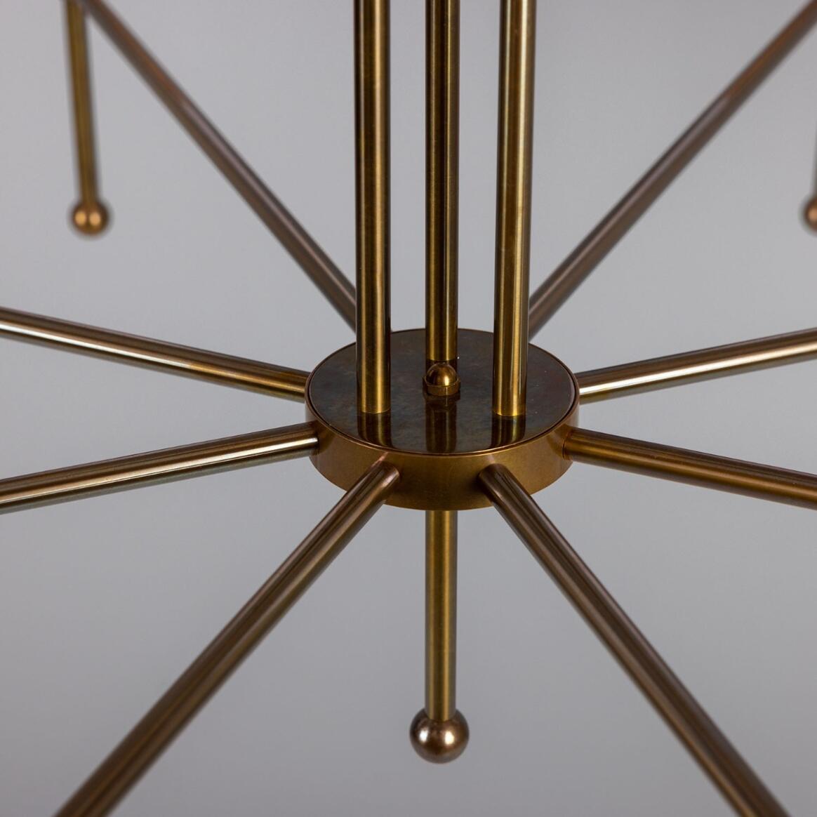 Close-up of the Sonoran Chandelier’s metallic gold structure, featuring multiple rods radiating from a central circular hub, set against a plain gray background.