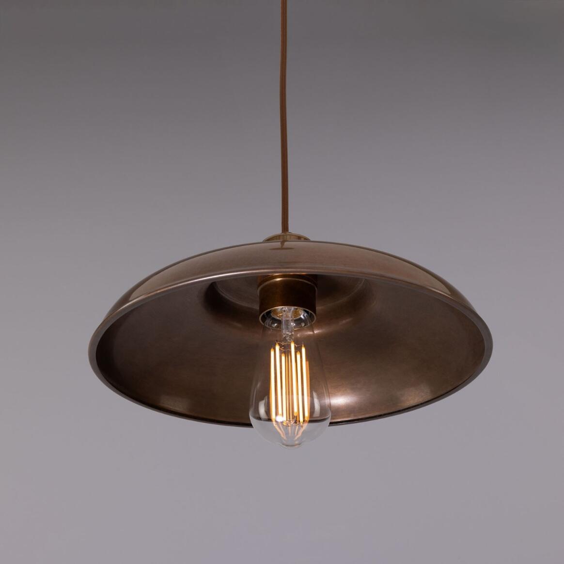 An Industrial Brass Pendant Light with an exposed vintage-style filament bulb hangs from a lighting chain against a plain gray background.