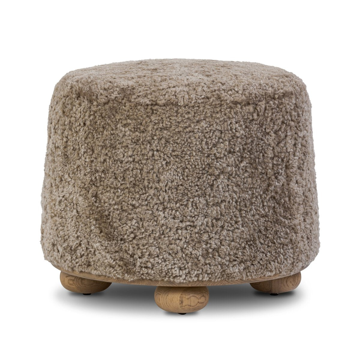 The Taupe Shierling Ottoman features a round design, soft textured beige upholstery, and four short wooden legs.