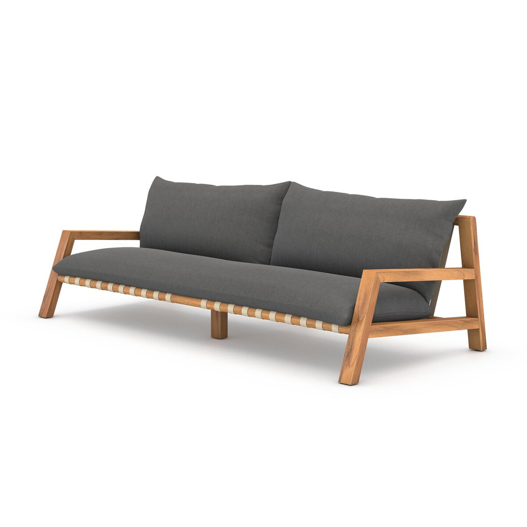The Wood Plank Outdoor Sofa features a FSC-certified teak frame in a natural finish, open sides, angled legs, and thick charcoal seat and back cushions for a stylish, contemporary outdoor look.