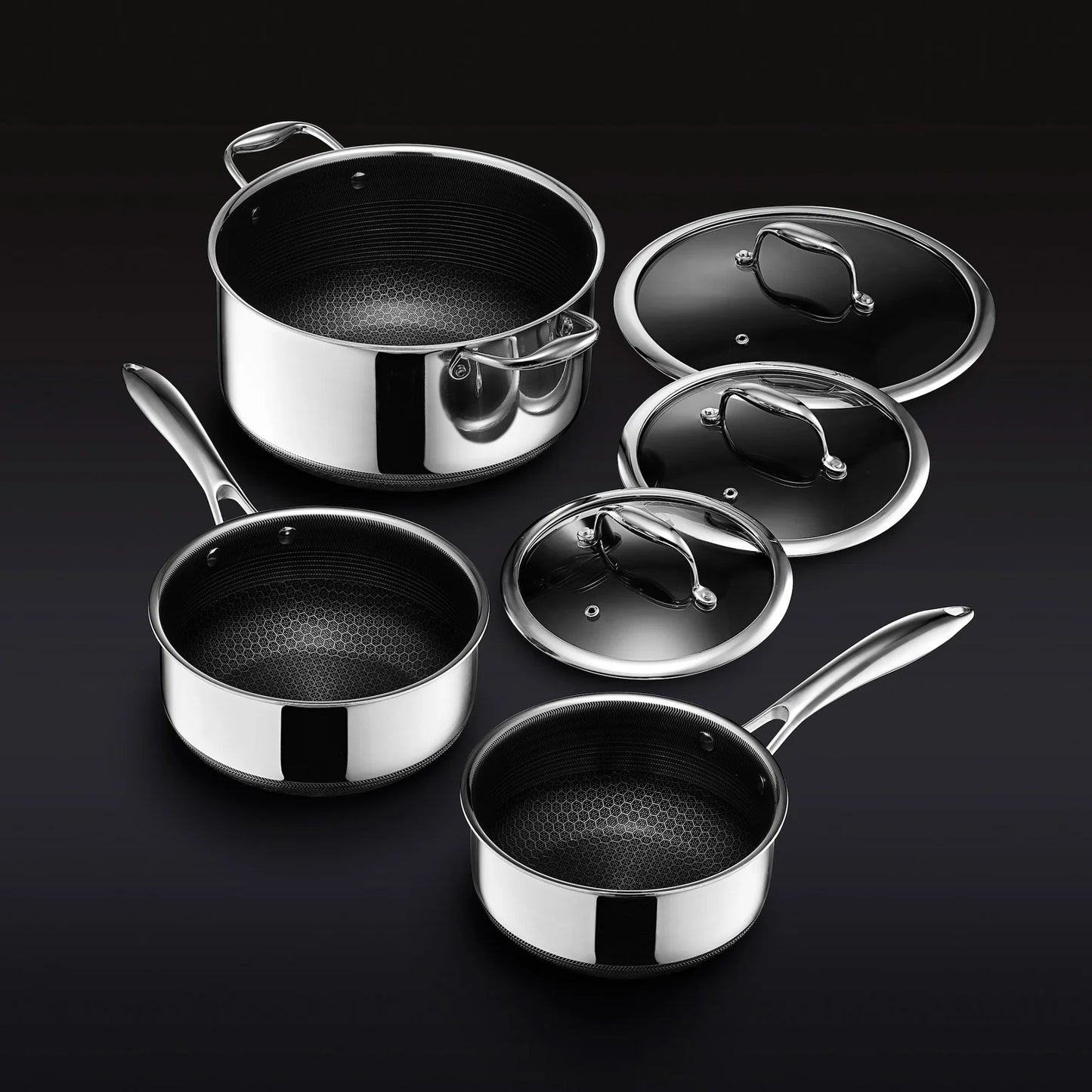 The Hexclad Pot Set with Lids features three stainless steel saucepans, each with a shiny exterior, hexagonal-patterned black nonstick interior, sturdy metal handles, and matching lids, all shown on a black background.