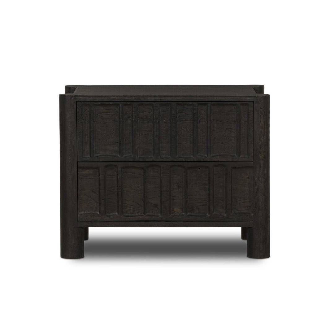 The Primitive Nightstand, crafted from cocoa-finished oak, features two drawers with vertical organic carvings and sleek cylinder legs, displayed against a white background.
