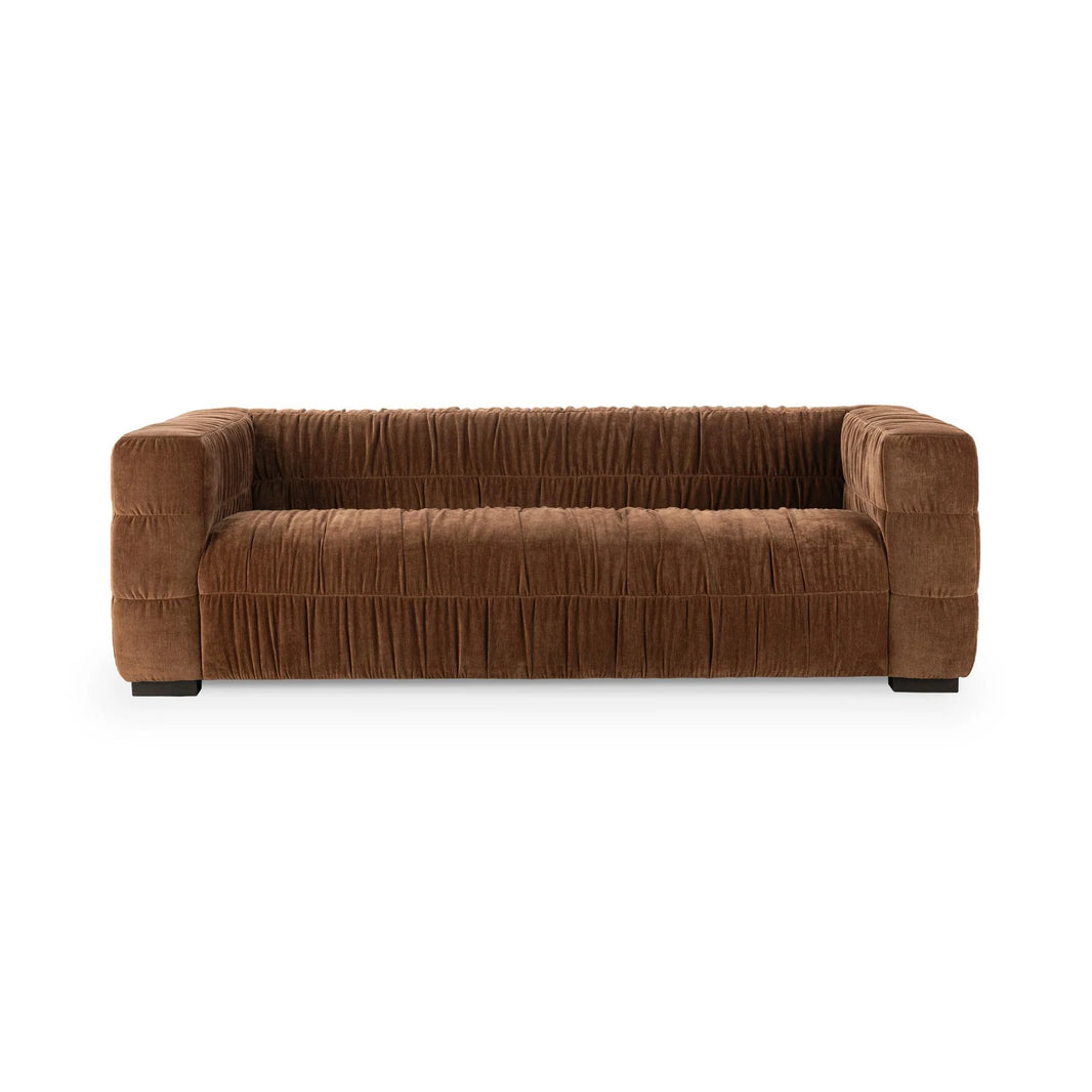 The Ruched Upholstered Sofa features wide blocky arms, a low backrest, and pleated brown upholstery that highlights modern luxury and artistry, set against a plain white background.