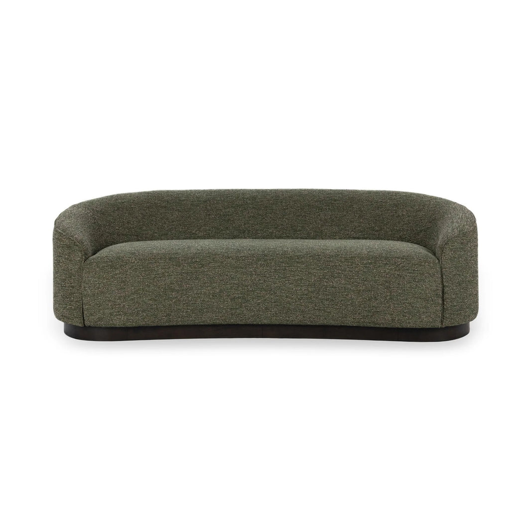 The Curved Sofa showcases a modern sculptural design with dark green upholstery, low rounded arms, and a sleek black base, displayed against a plain white background.
