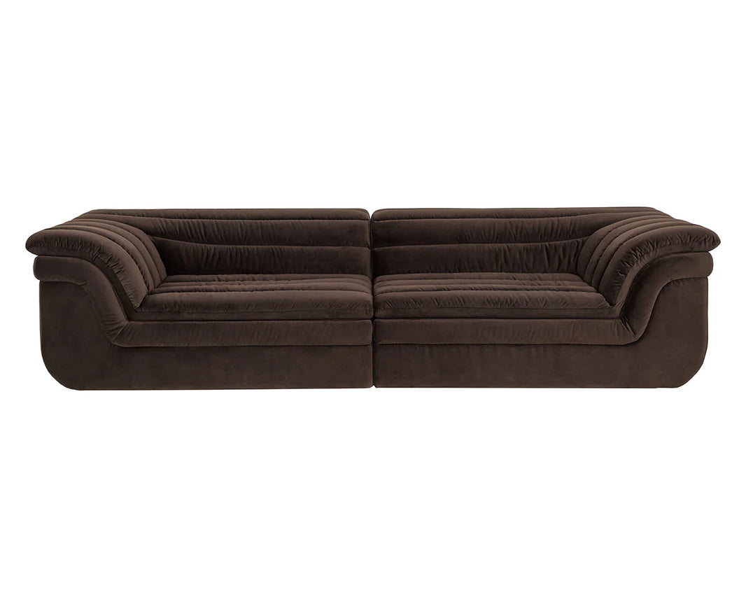 The Deep Channel Sofa is a modern, low-profile piece in dark brown velvet with deep cushioned seats and rounded, layered armrests—perfect for a stylish living room. Shown here against a white background.