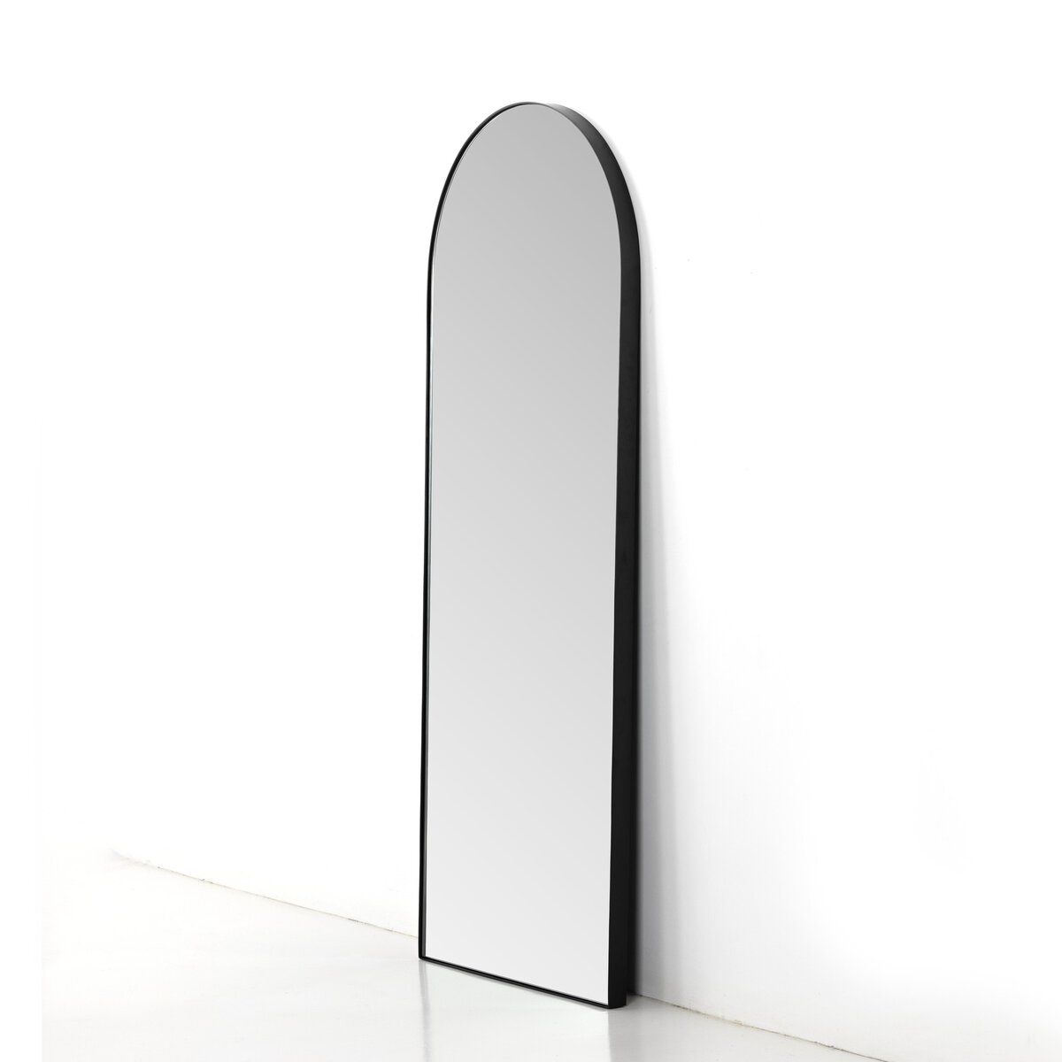The Georgina Floor Mirror features a tall, arched design with a slim black frame. Leaning against a white wall, its size is perfect for placement near a 32x80 door or in rooms needing an extra touch of style.