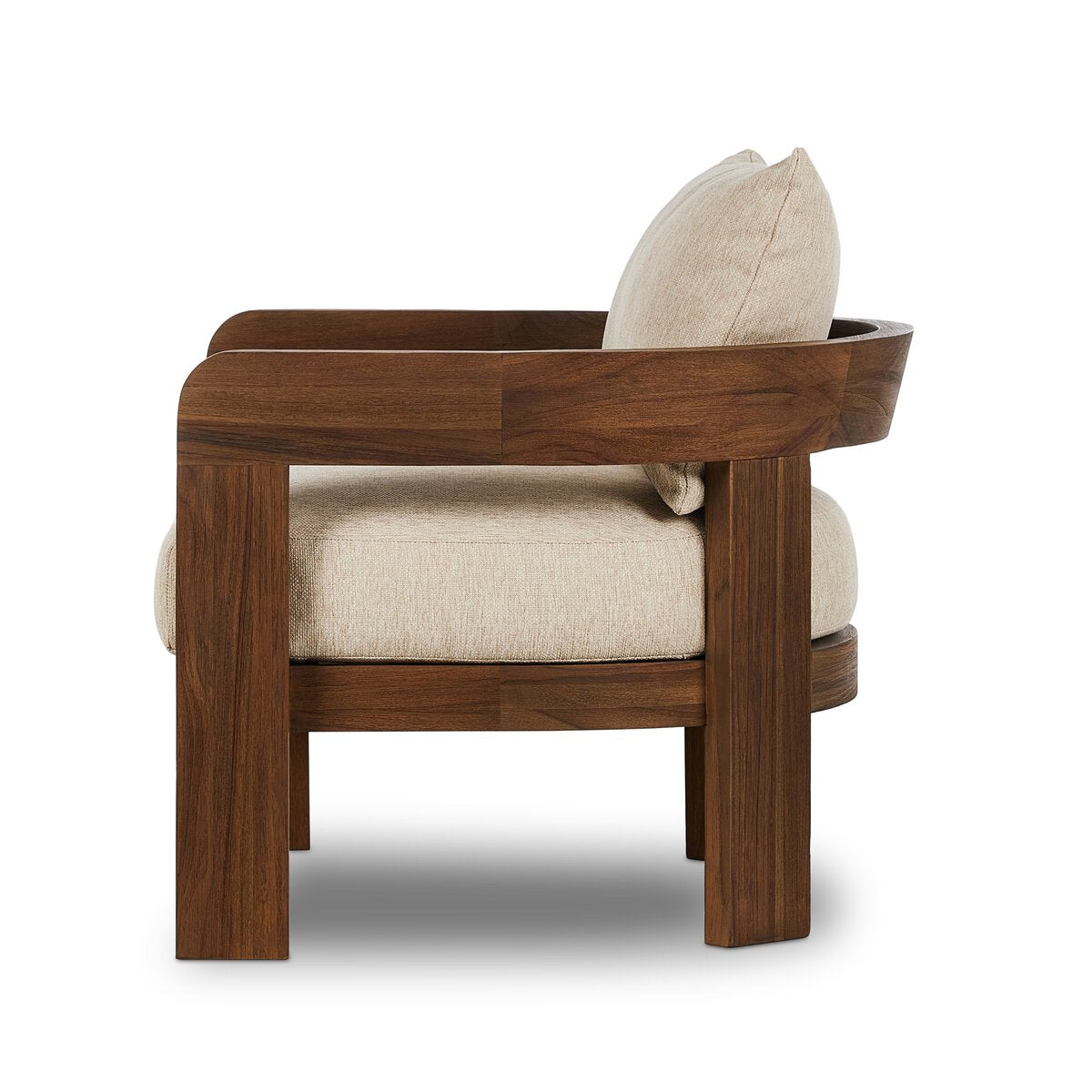 A side view of the Barrel Back Outdoor Chair, featuring a teak frame, curved backrest, and warm beige upholstery on the seat and back cushion, shown against a white background.