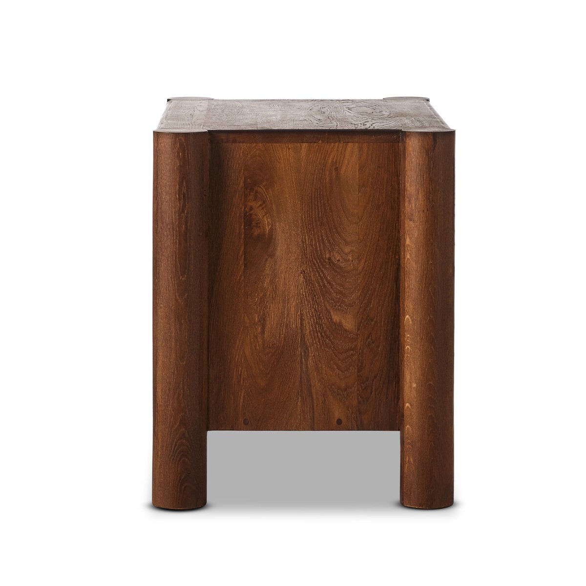 The Primitive Nightstand features organic carving, cylinder legs, and a smooth rectangular surface. Crafted from cocoa-finished oak, it highlights rich dark brown tones and visible grain against a plain white background.