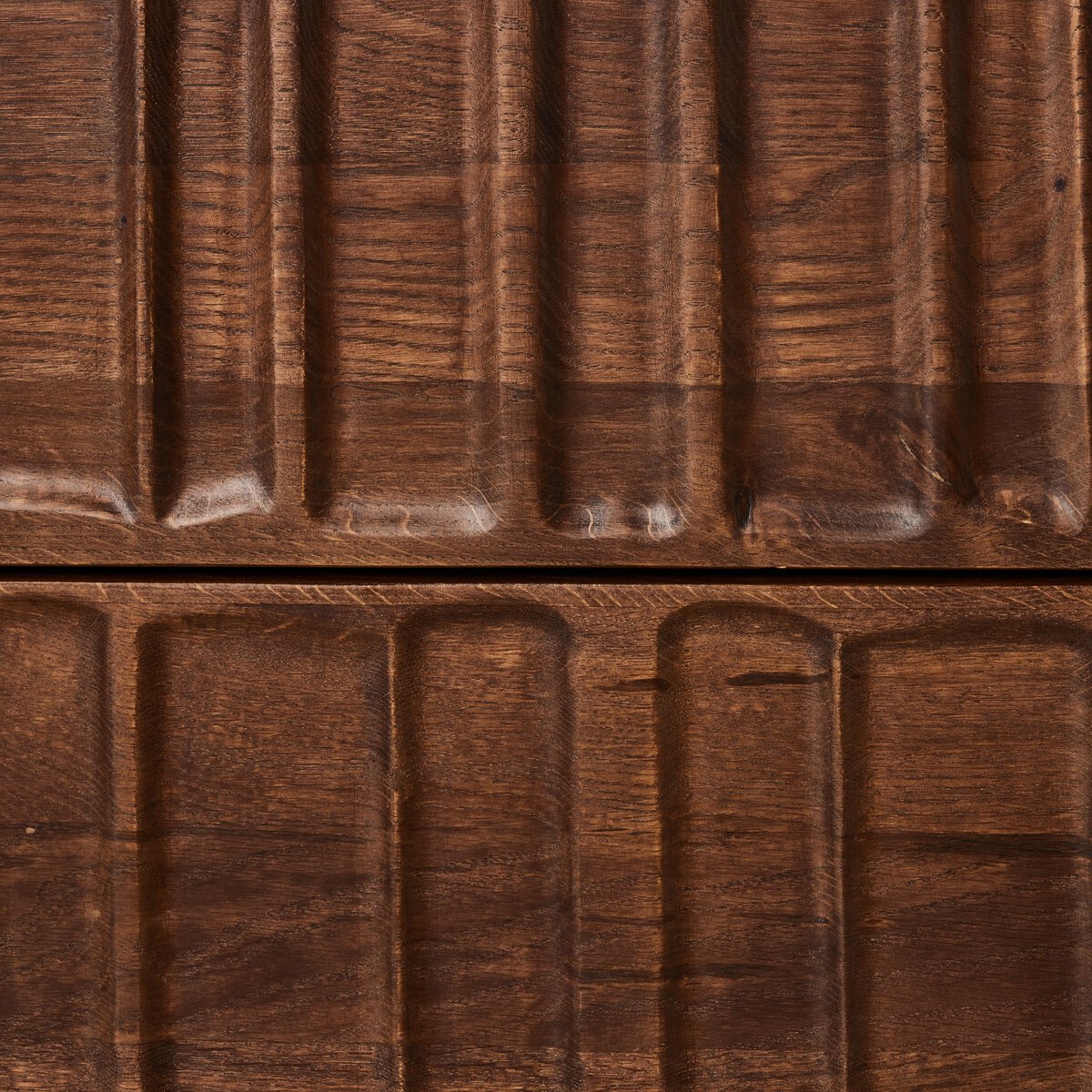 Close-up of the Primitive Nightstand’s cocoa-finished oak surface, featuring carved horizontal and vertical grooves. The image highlights where two panels meet, showcasing the artistry of its organic carving.