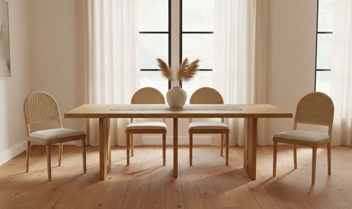 A set of Natural Oak Dining Chair - Set of Two sits by large windows with sheer curtains, offering comfort and style. A vase of dried pampas grass enhances the neutral decor.