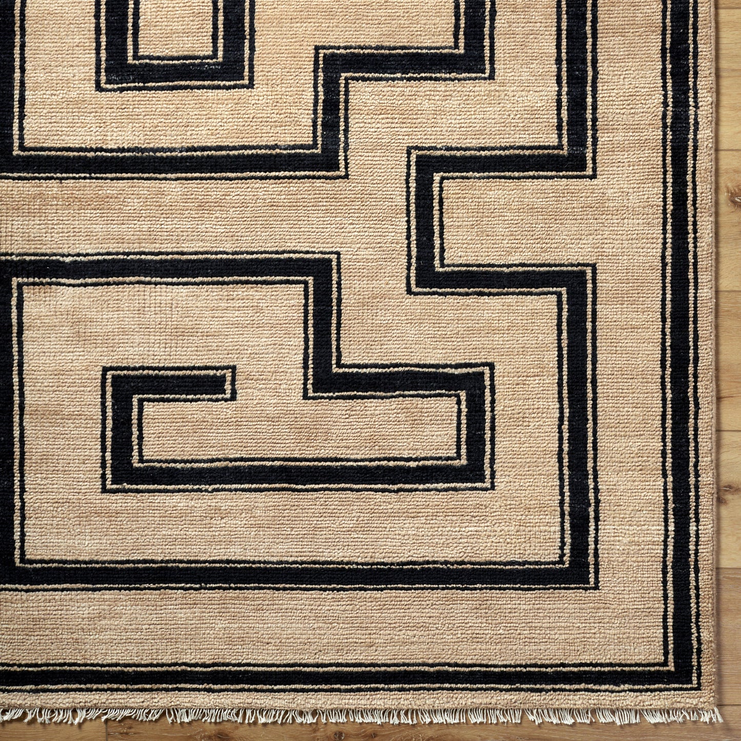 The Ivory/Black Geometric Maze Rug (8' x 10') features a maze-like black pattern on an ivory background, fringed edges, and is shown on a wooden floor.