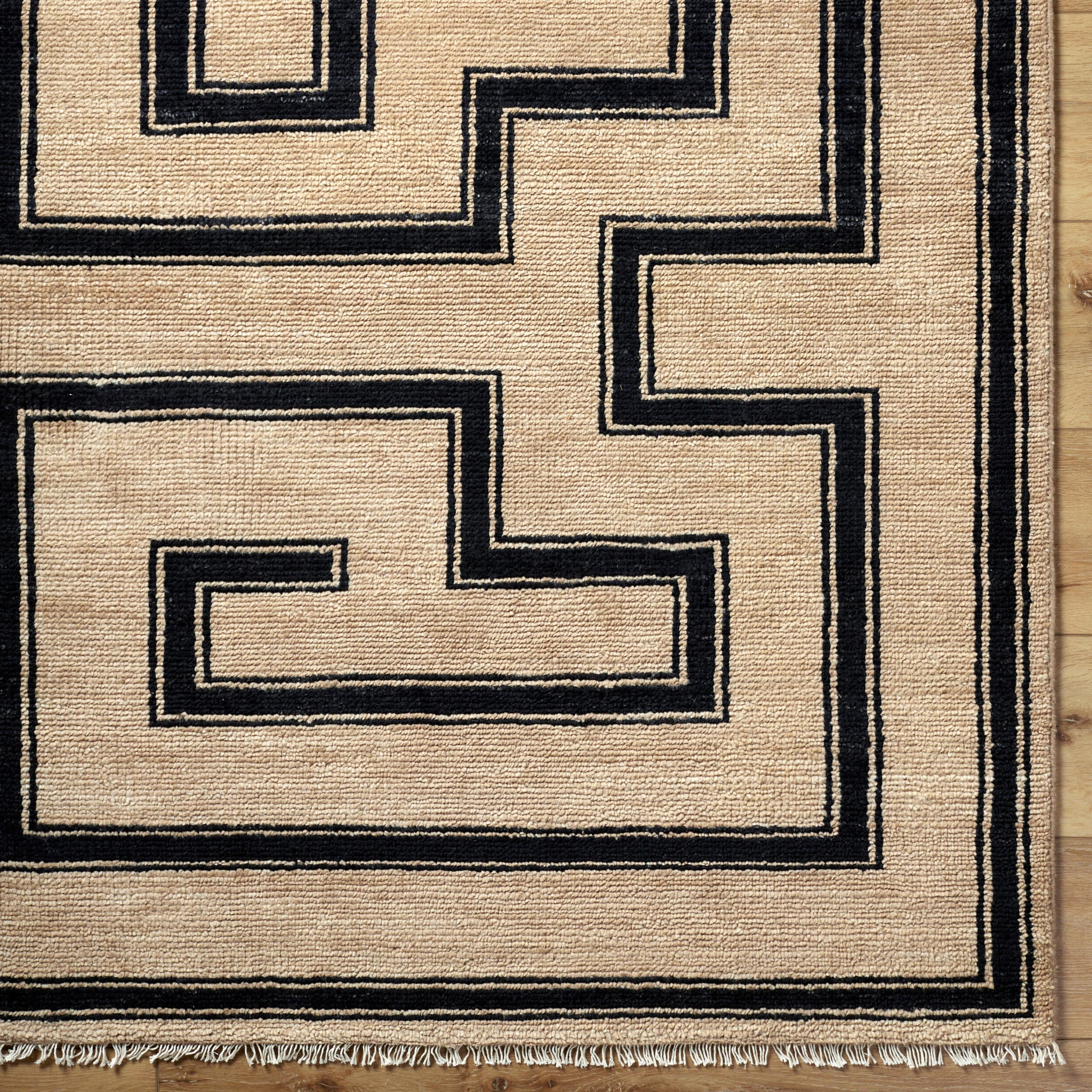 The Ivory/Black Geometric Maze Rug (8' x 10') features a maze-like black pattern on an ivory background, fringed edges, and is shown on a wooden floor.
