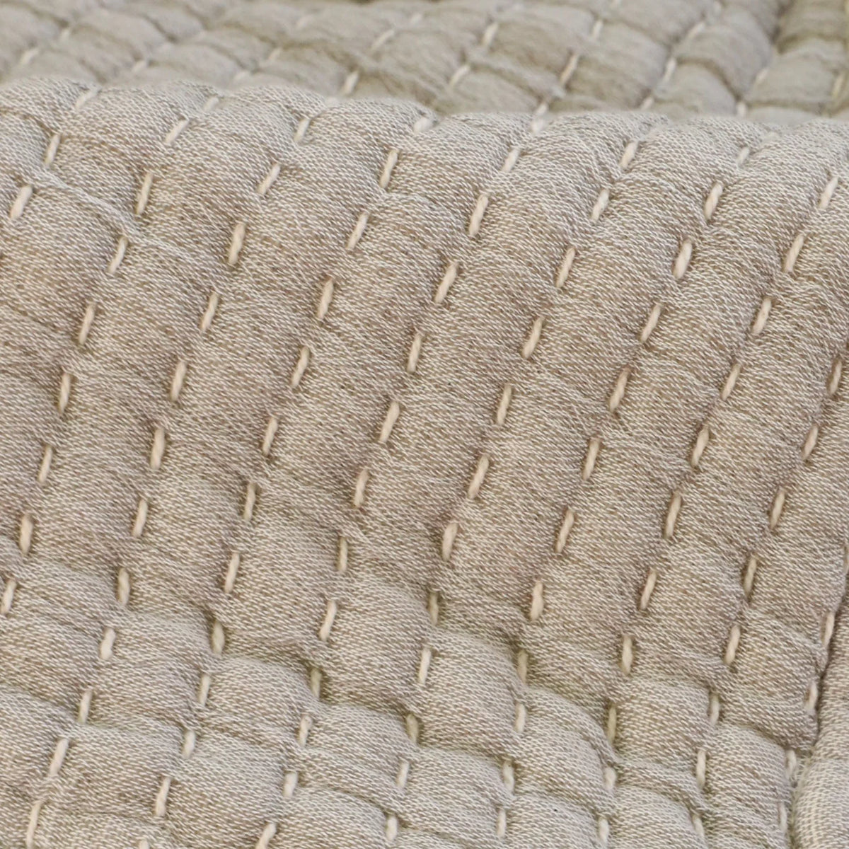 Close-up of cream cotton fabric with a quilted texture, featuring grid-like rows of evenly spaced, raised stitches. The material appears soft and the stitching forms a subtle, repeating geometric pattern. The Cream Cotton Oversized Throw Blanket measures 60 x 90 cm in overall dimensions, offering ample coverage for various uses.