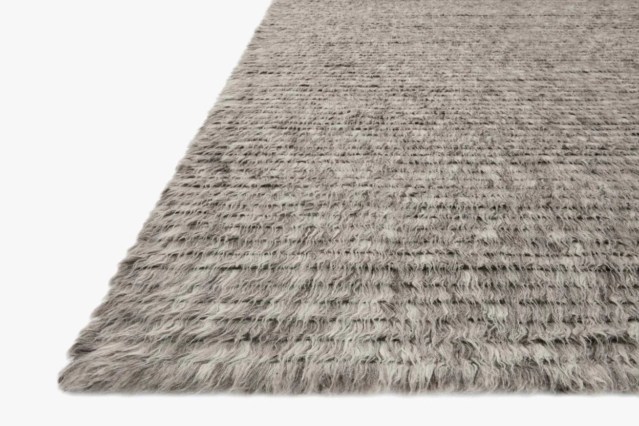 A close-up of the Hand Knotted Shag Grey Rug - 8'x10' shows its soft, plush shaggy surface and textured, slightly uneven fibers. With a cozy gray finish and plain white background, this rug adds comfort and style to any room.